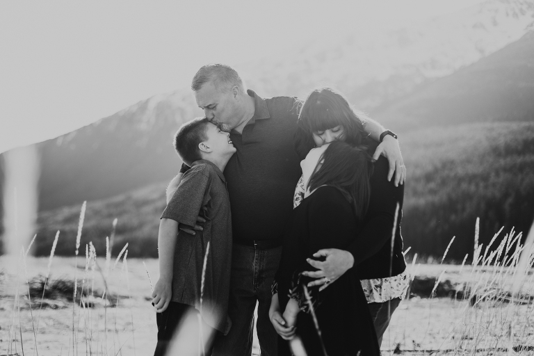 A black and white photo of the Calver family hugging each other while dad kisses his son on the forehead. 