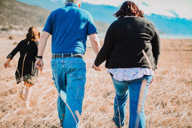 Mom and dad hold hands while walking through the tall grasses of the Dyea Flats. 