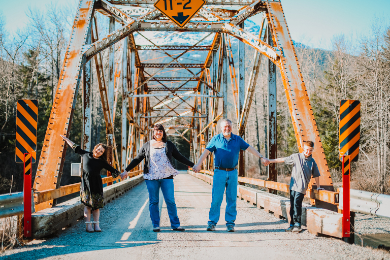 The Calver family holds hands, while standing across a bridge in Dyea. 