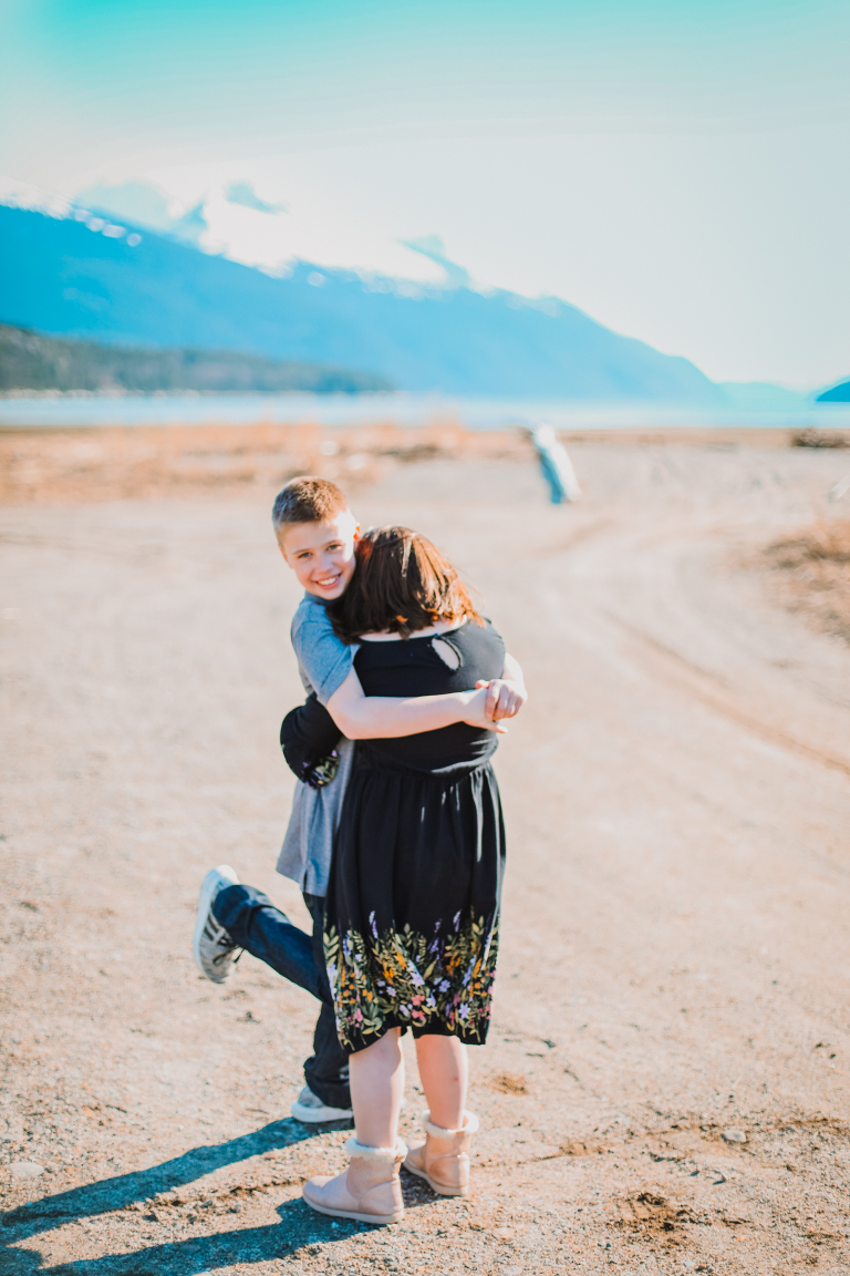 A brother gives his sister a hug and kicks up his foot in Alaska. 