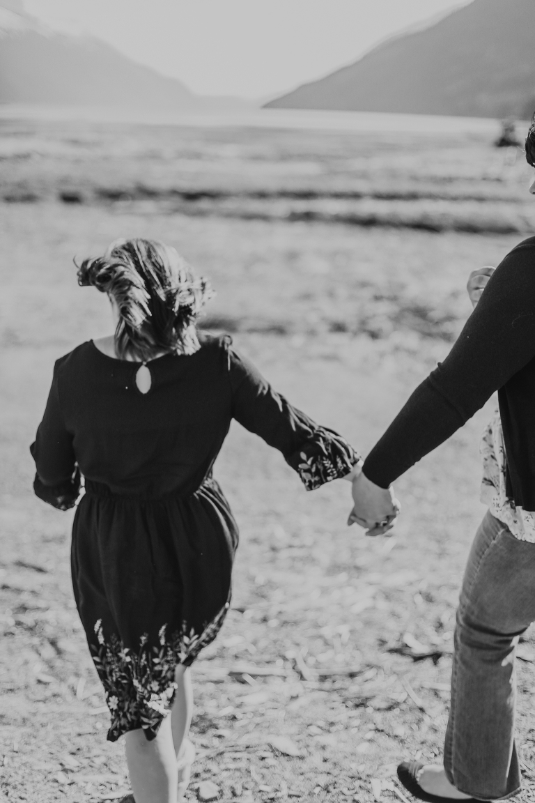 A black and white photo of mom and daughter holding hands while walking along the beach. 