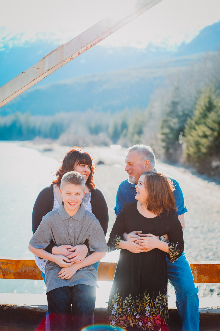 The Calver family laughs together while the kids sit on their parent's lap on the bridge. 