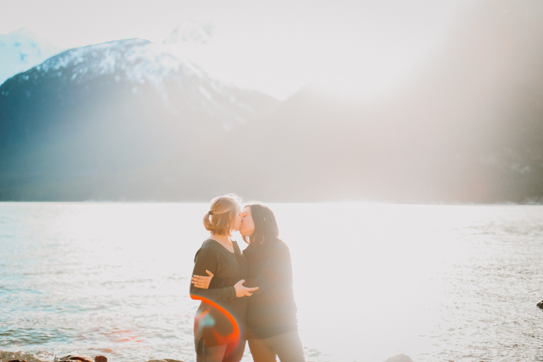 A young lesbian couple kissing on a sunny beach in Skagway, Alaska. 