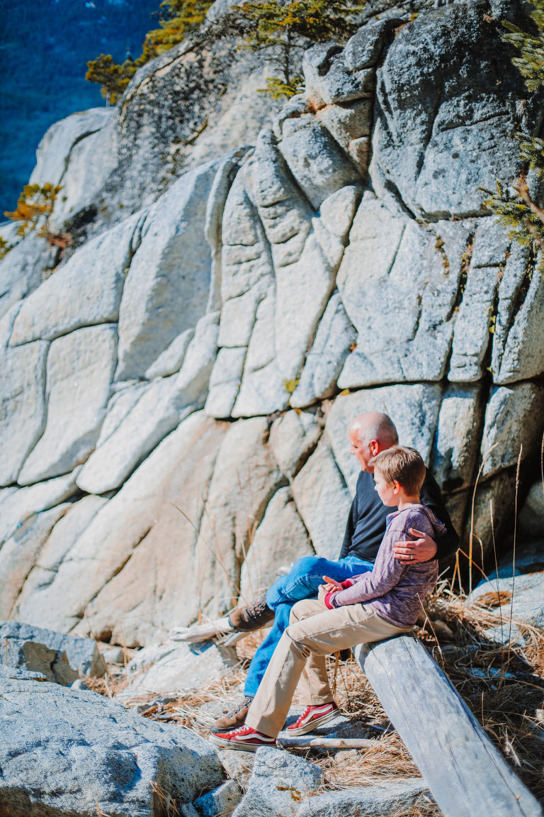 Dad puts his arm around his son's shoulder while sitting on a log at Smuggler's Cove.