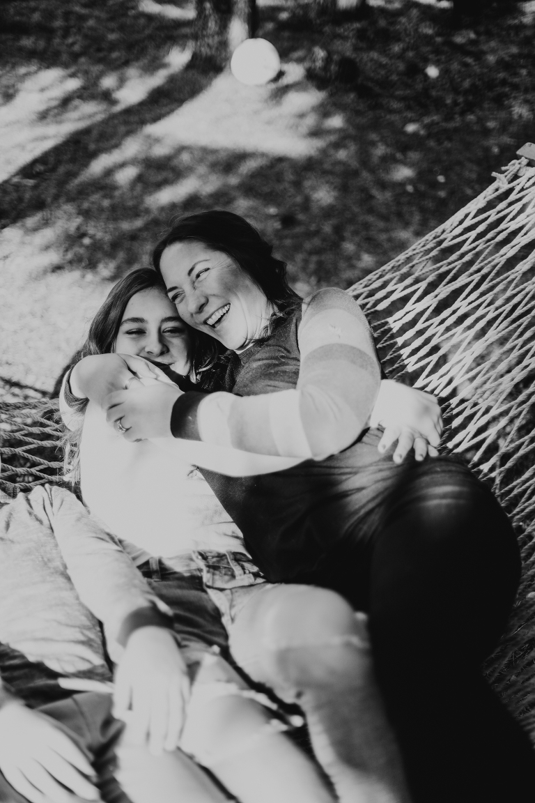 Mom laughs and cuddles her daughter in a hammock. 