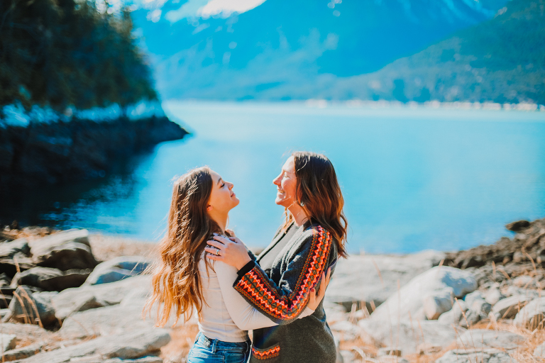 Mom and daughter face each other and hug on a rocky Alaskan beach. 