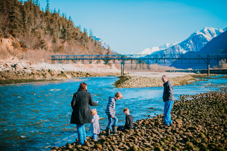 A young family stands alongside the Skagway River looking for pebbles to throw. 