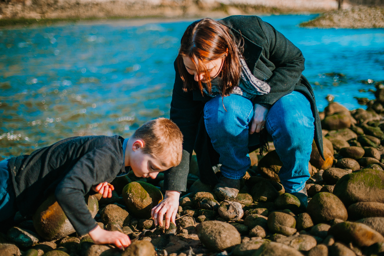 A mom and son look for pebbles to throw into the river. 