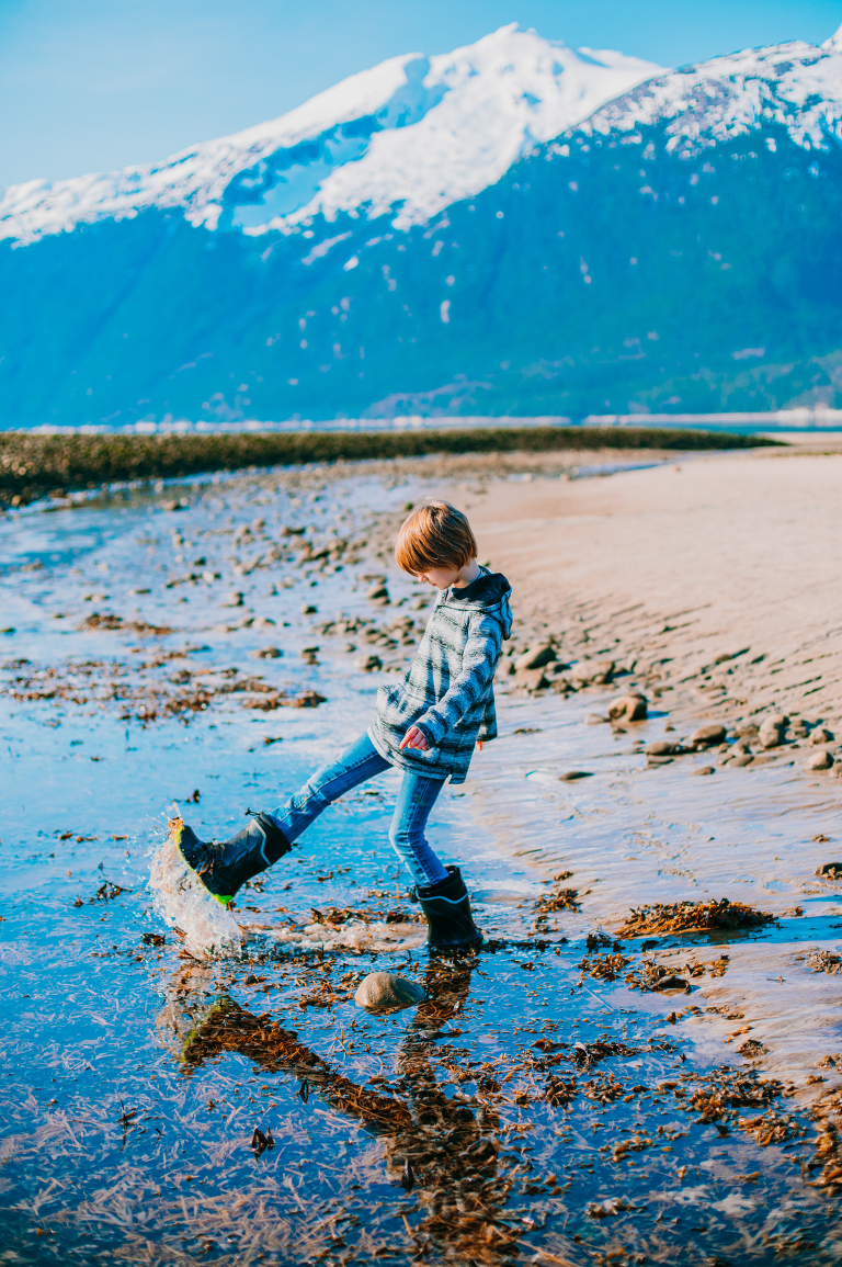 A young boy kicks up water on a sandy beach in Skagway, Alaska. 