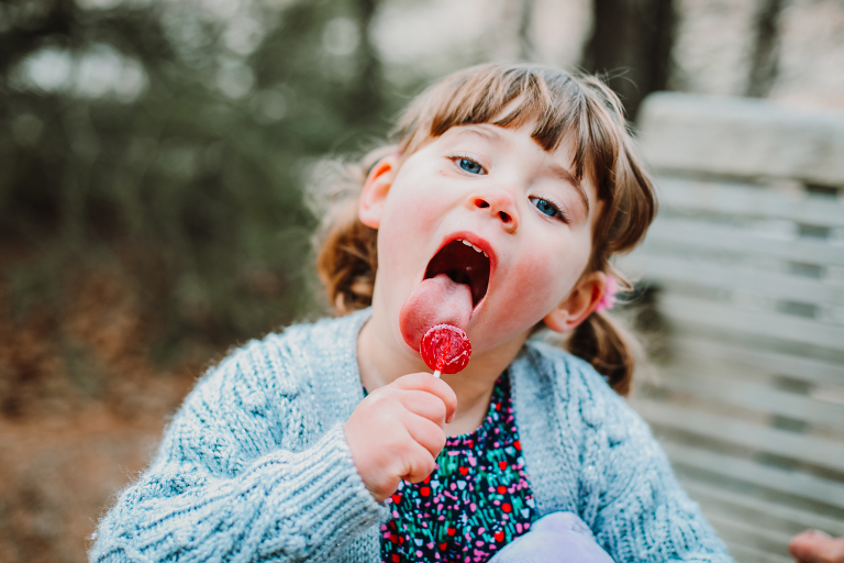 Little girl licks her lollipop and looks right into the camrea. 