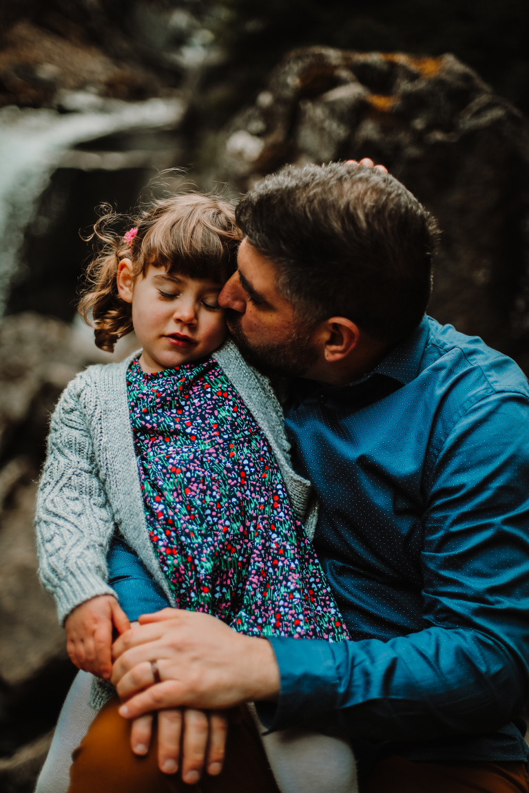 Dad gives his daughter a kiss in the cheek, while she closes her eyes. 