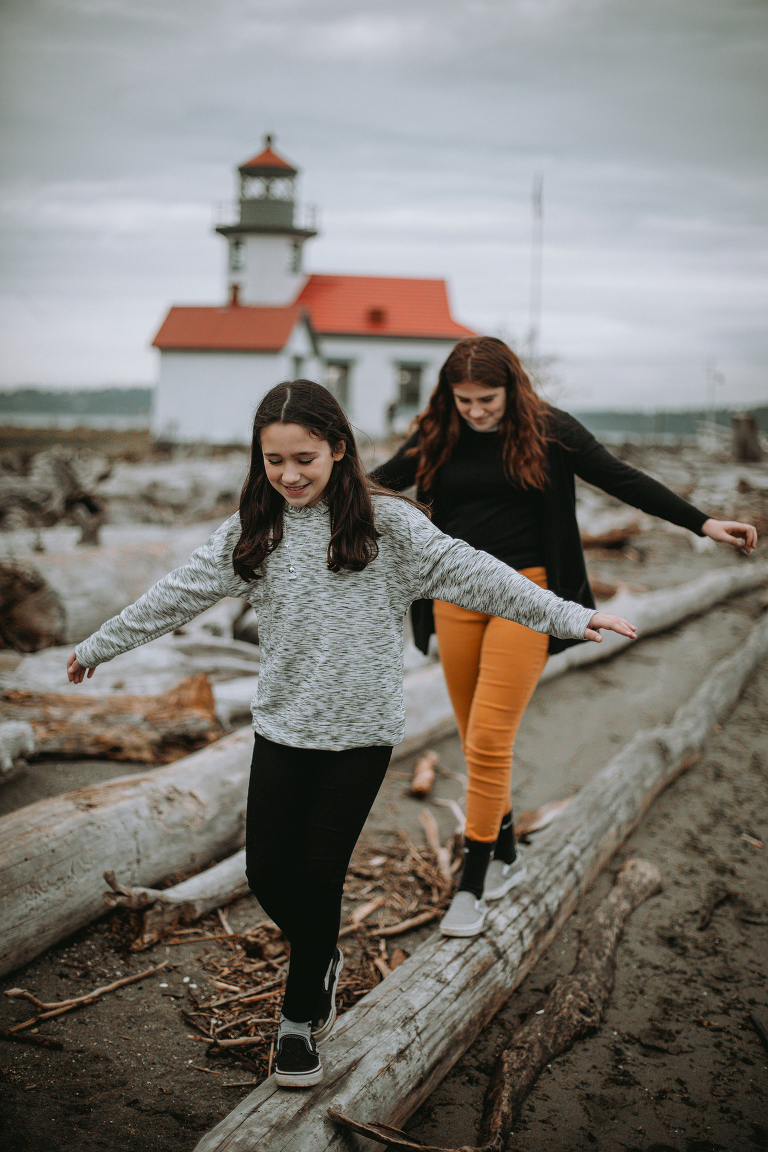 The youngest Myers girls walk along a log in front of the Point Robinson lighthouse on Vashon. 