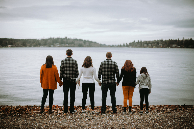The Myers Family stands hand in hand on the shores of Jensen Point on Vashon Island.