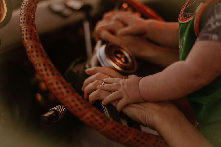 Baby puts hands on the steering wheel of a seventies van. 