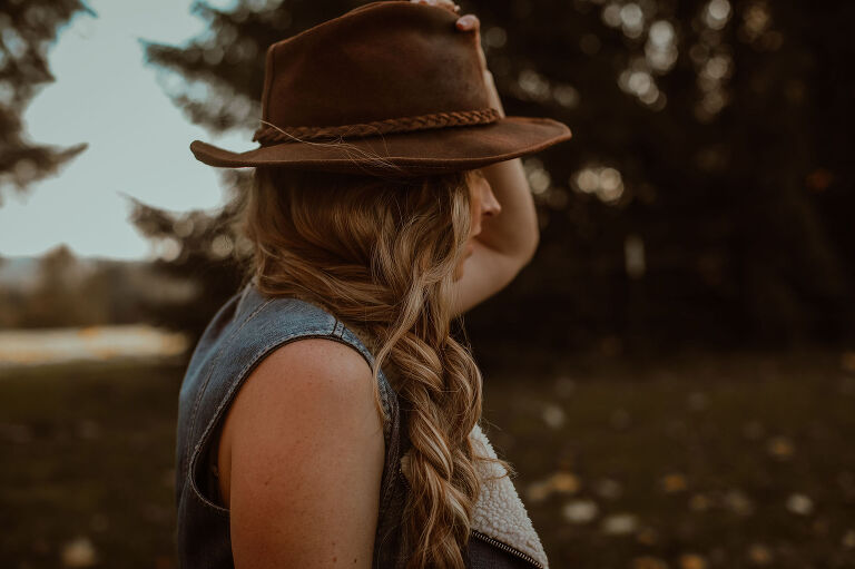 Woman with braid holds a leather hat on her head, walking away from the camera. 