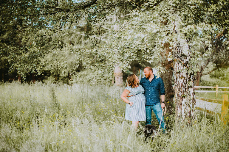Mallory and Mike lean against a beautiful tree in a field of wildflowers.