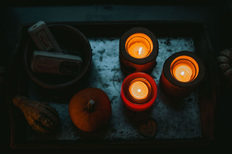 Lit candles and pumpkins sit in a windowsill. 