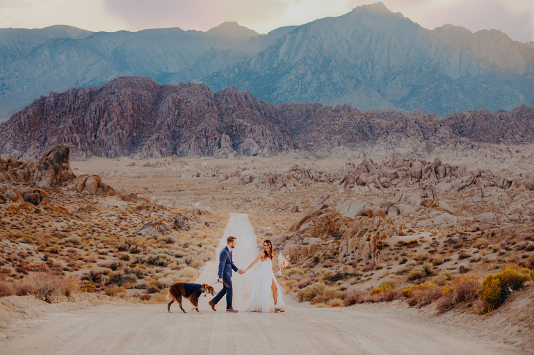Paul and Kristi walk across Movie Road in Alabama Hills, holding hands with dog Wiley trailing behind.