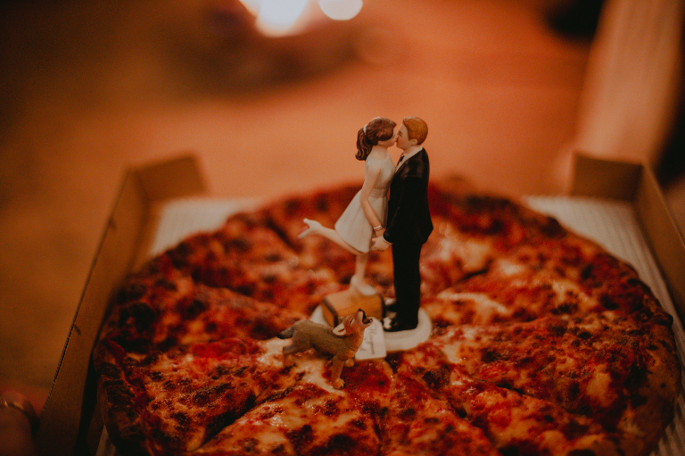 A cake topper of the bride and groom, accompanied by a coyote, sits on top of their wedding pizza after their Alabama Hills elopement.
