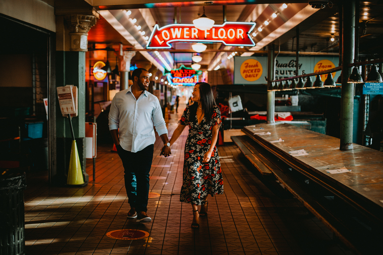 Derek and Alexis walk underneath the neon signs of Pike Place Market.